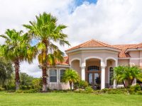New tile-roofed home with palm trees and lush tropical foliage. Florida.
